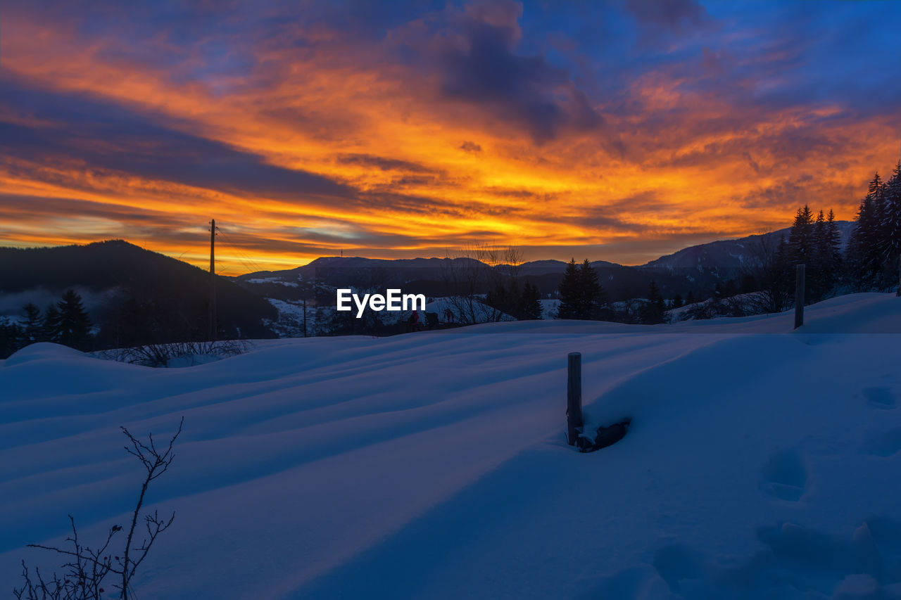 SCENIC VIEW OF SNOW COVERED FIELD AGAINST SKY AT SUNSET