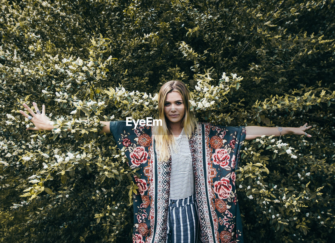 PORTRAIT OF YOUNG WOMAN STANDING AGAINST TREE