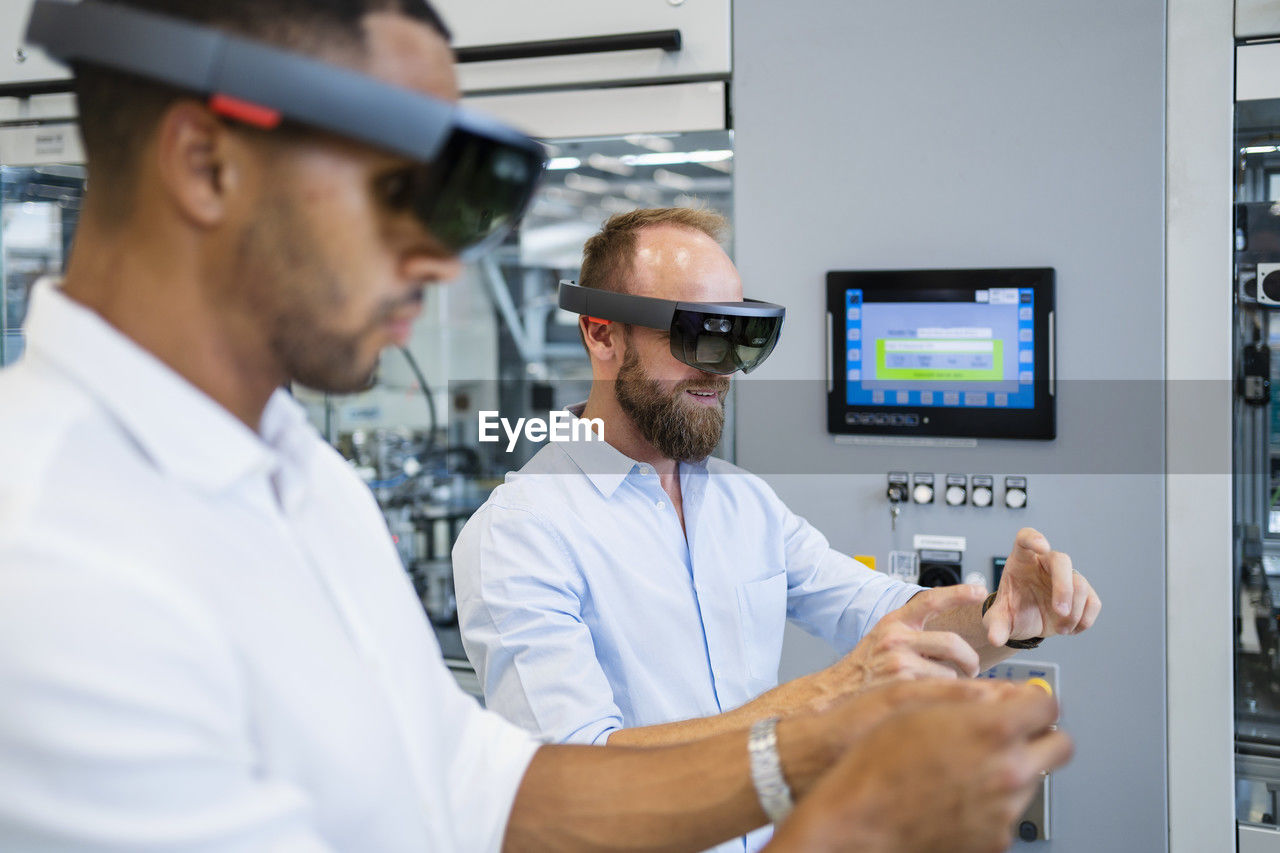 Two technicians wearing augmented reality glasses in a factory and gesturing