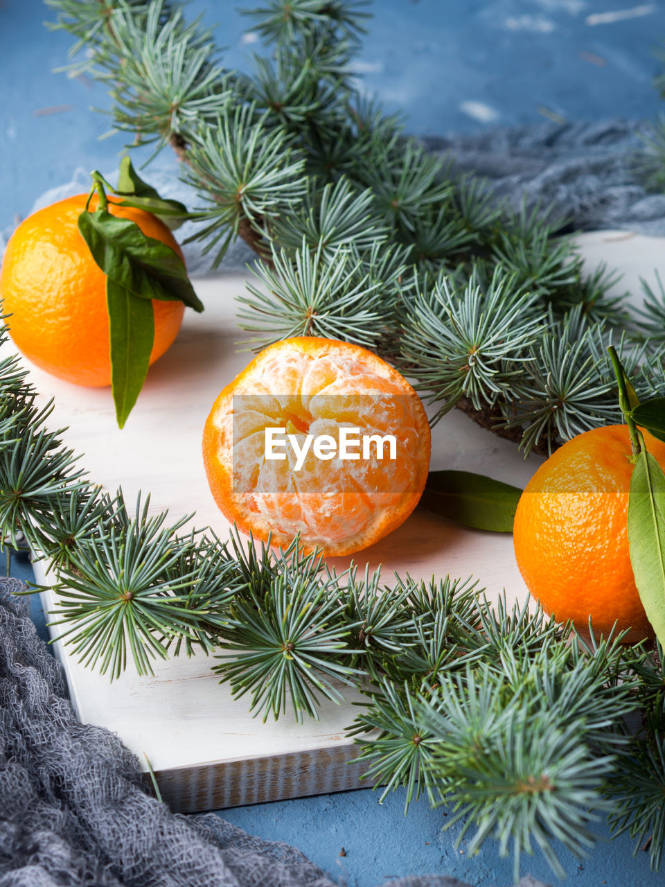 Winter tangerines frame on white rustic wooden board with spruce branches on blue background