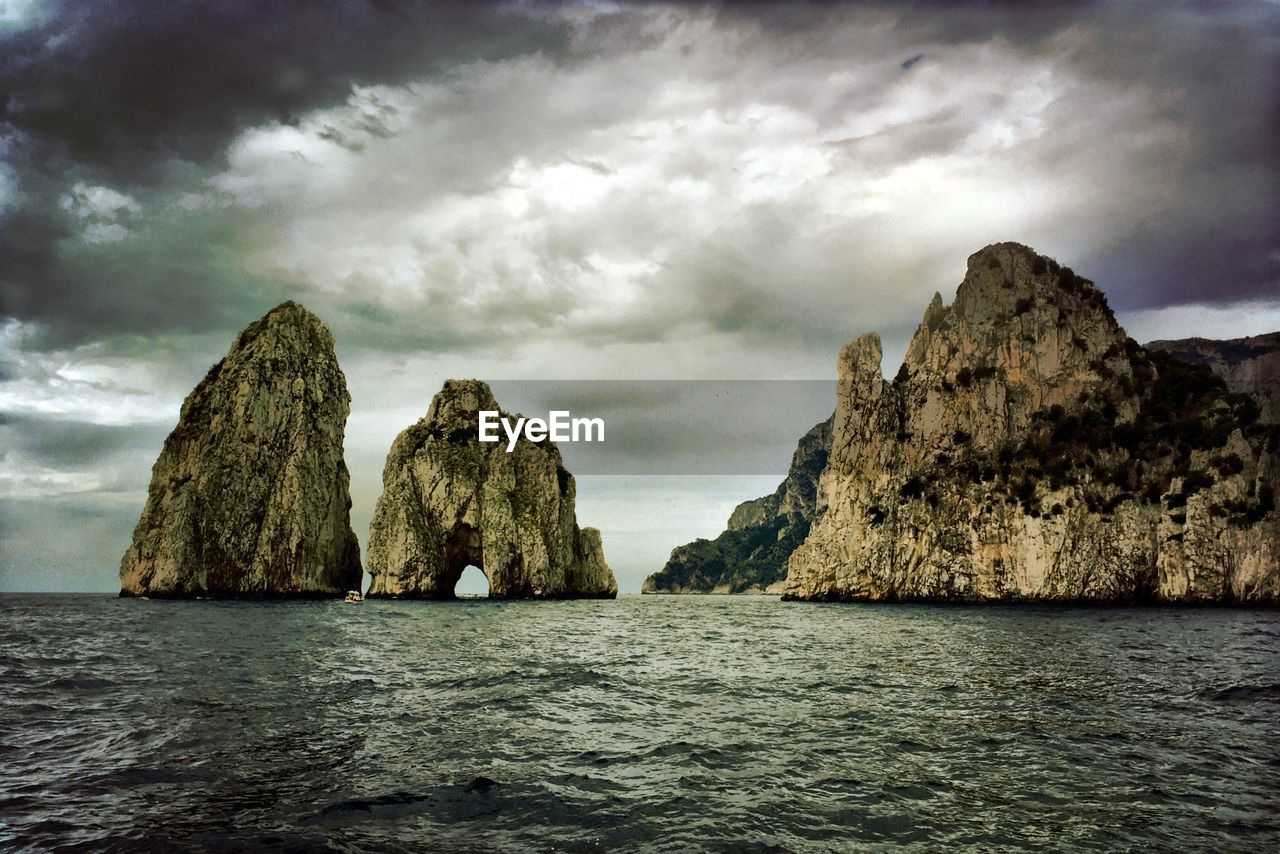 Rock formation on sea against cloudy sky