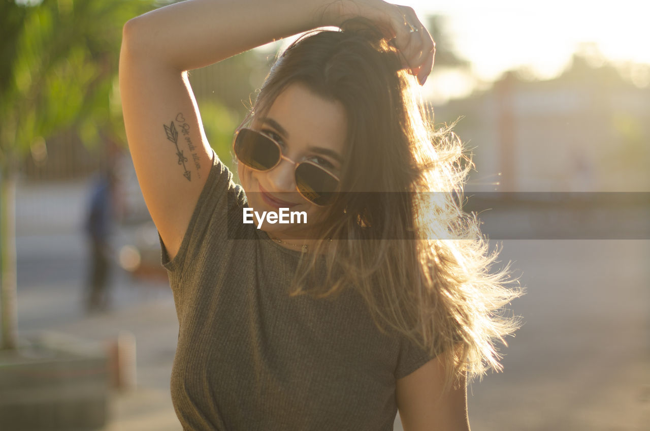 PORTRAIT OF YOUNG WOMAN WITH SUNGLASSES IN BACKGROUND