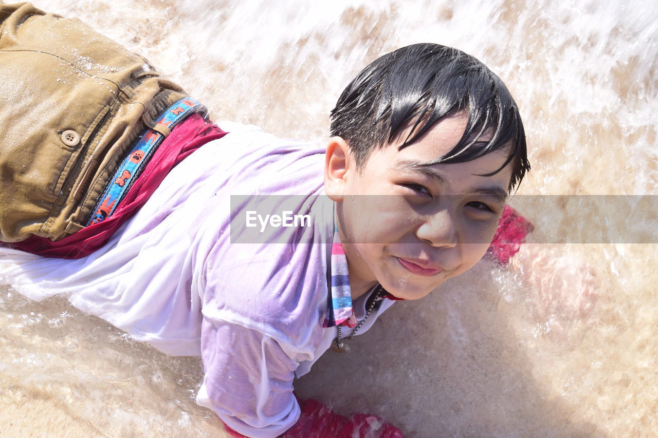 High angle portrait of smiling boy lying at shore