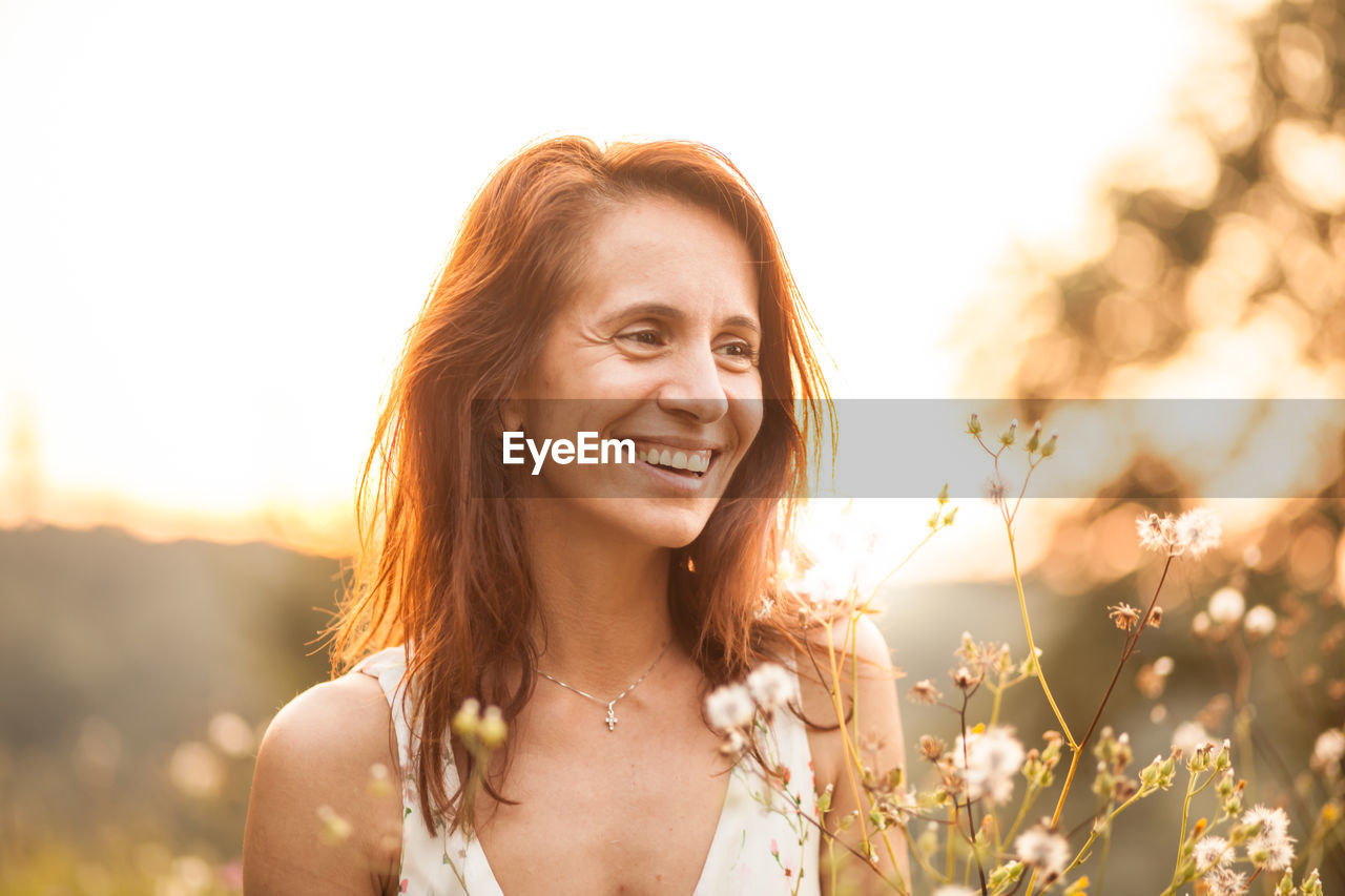 Smiling woman looking away against sky during sunset