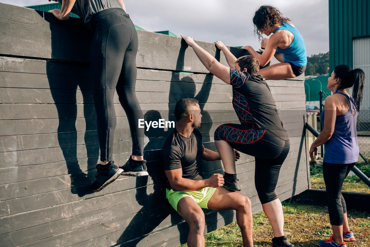 Friends climbing wooden wall while exercising outdoors