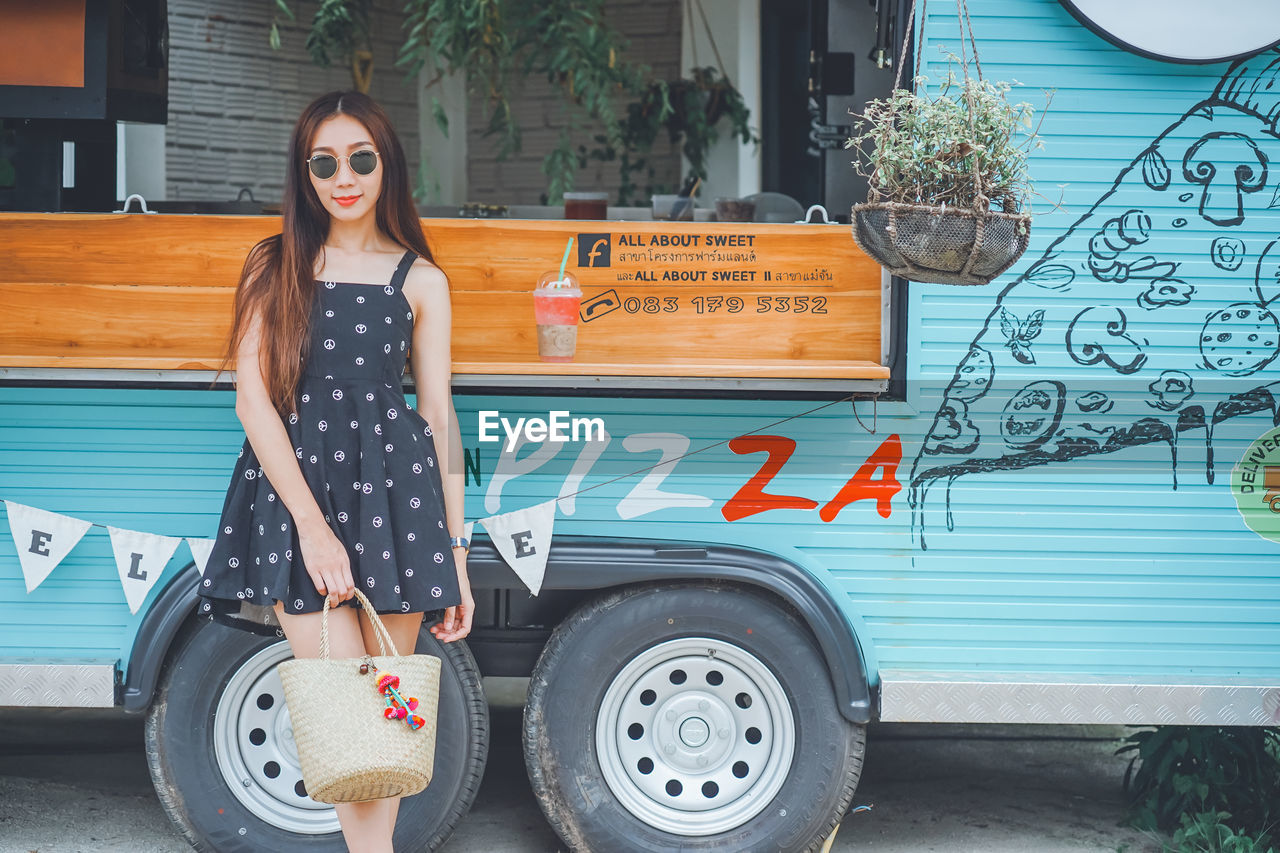 Young woman wearing sunglasses standing against food truck