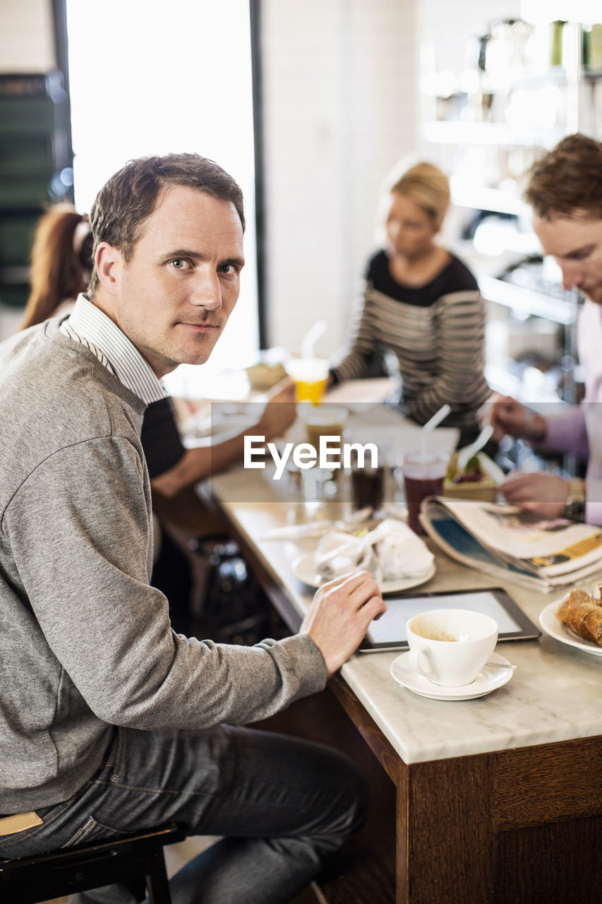 Portrait of mid adult businessman with colleagues having breakfast in office restaurant