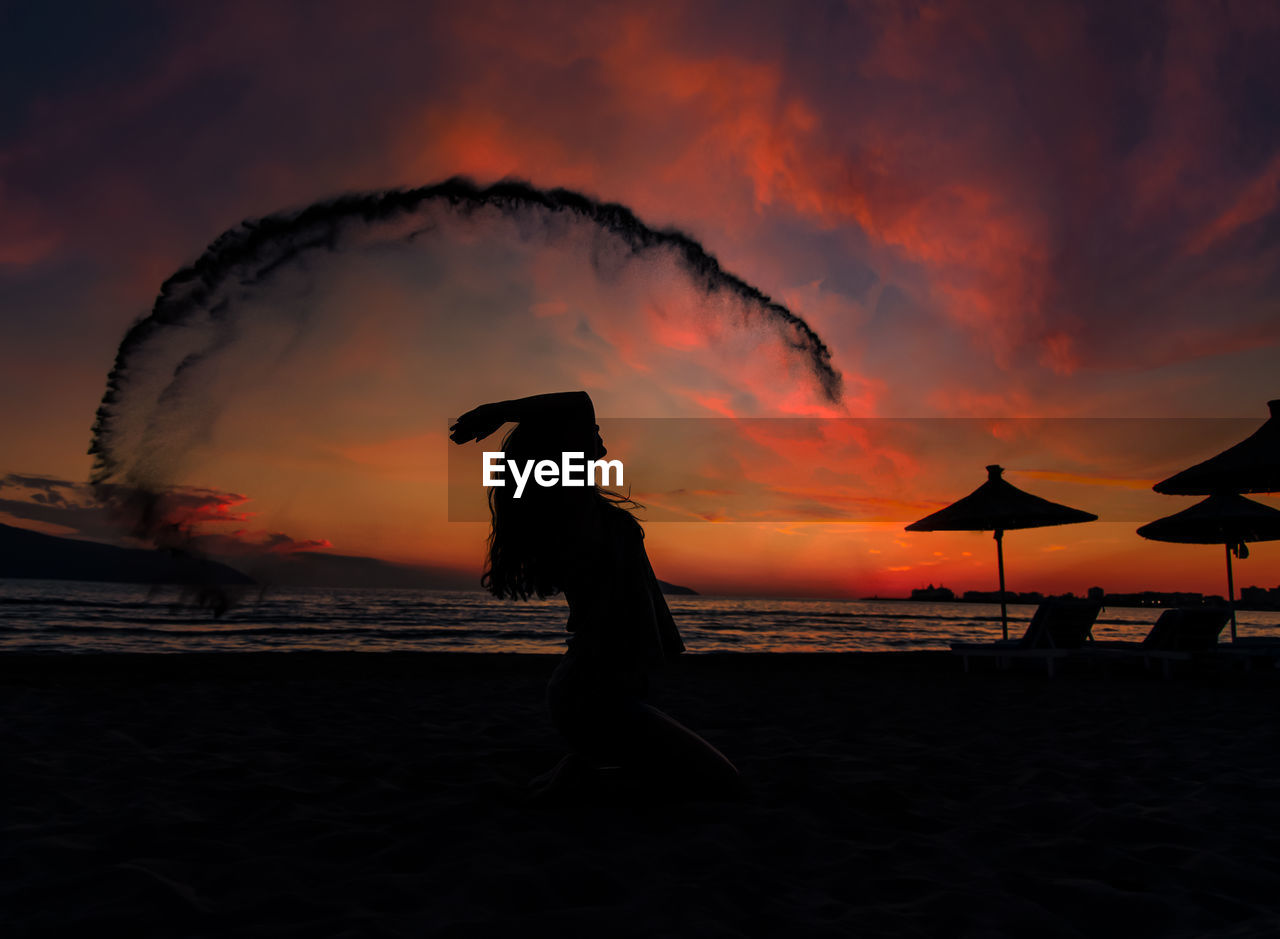 Silhouette woman standing at beach against sky during sunset