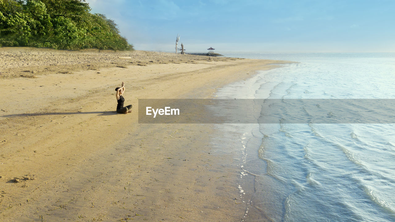 Woman exercising at beach against sky