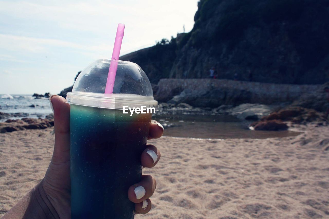 Cropped hand of woman having drink in disposable cup at beach