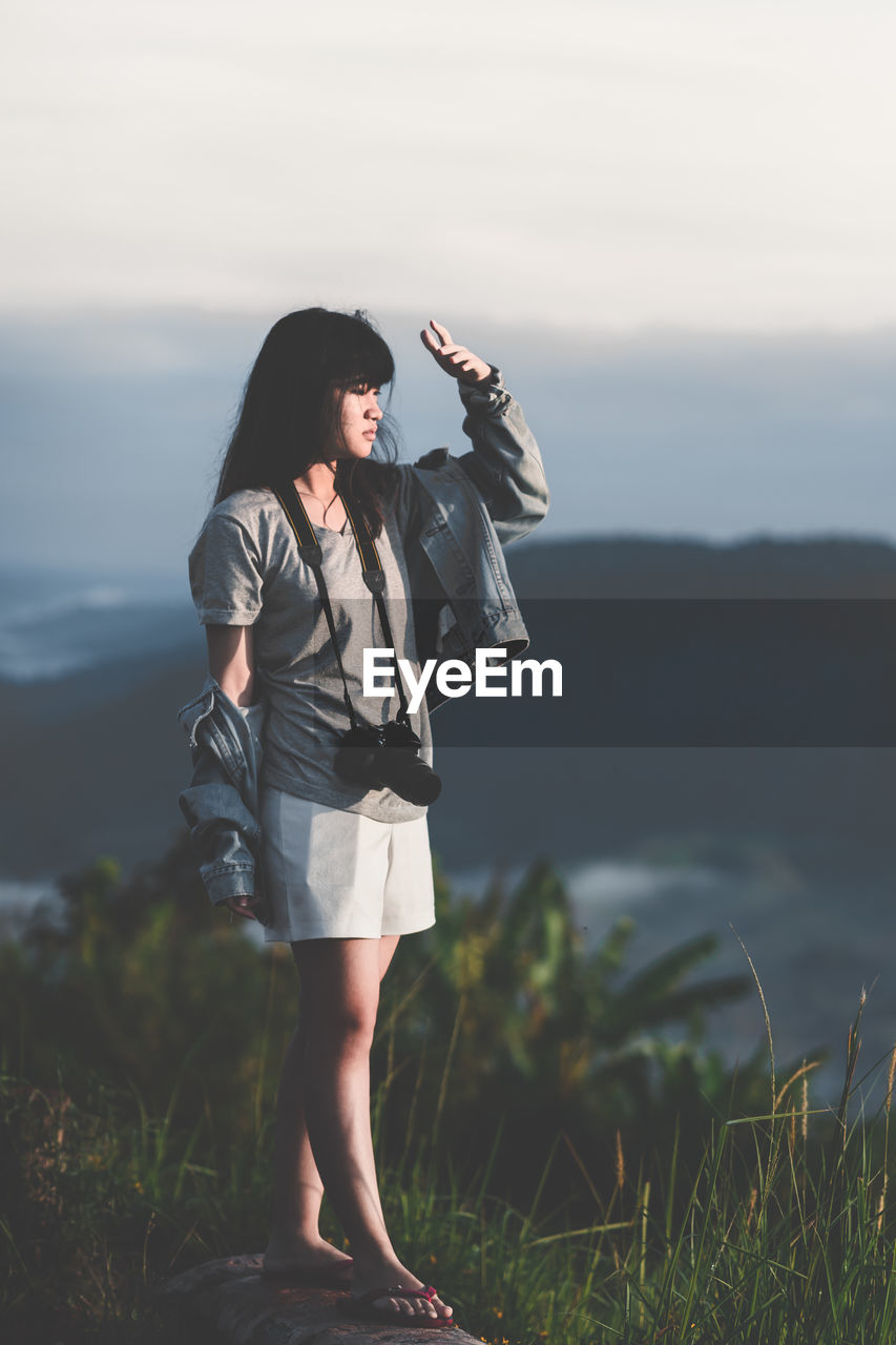 Young woman with digital camera standing against sky