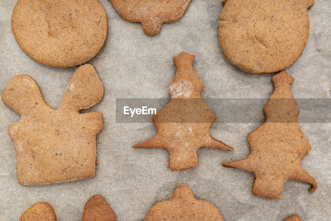 Baked gingerbread cookies in various shapes without decorations, lying on baking paper, top view.