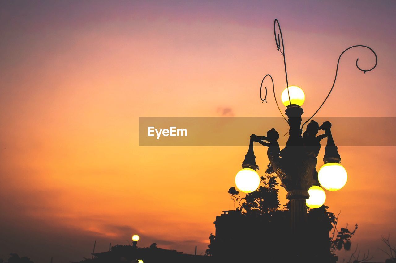 Low angle view of illuminated street light against orange sky at dusk