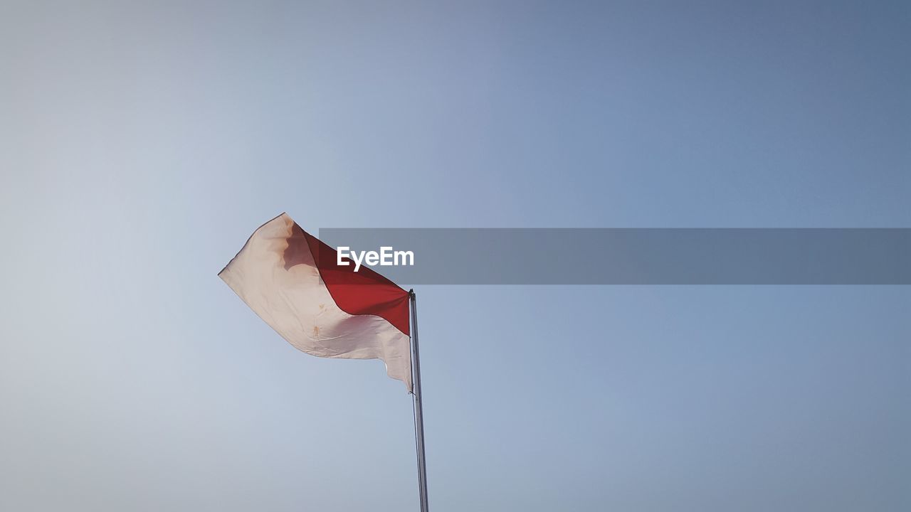 Low angle view of indonesian flag against clear blue sky