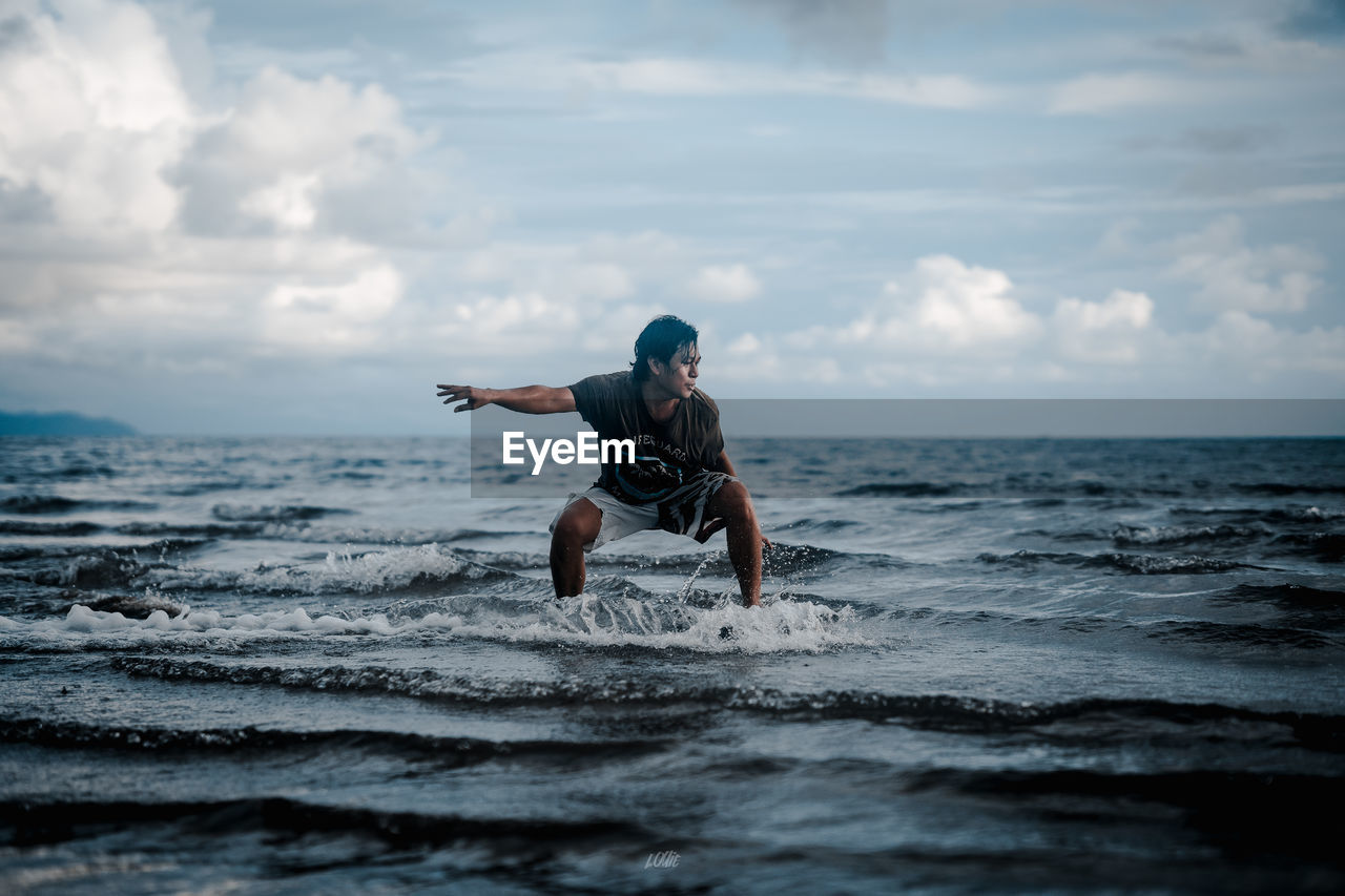 FULL LENGTH OF MAN SURFING IN SEA AGAINST SKY