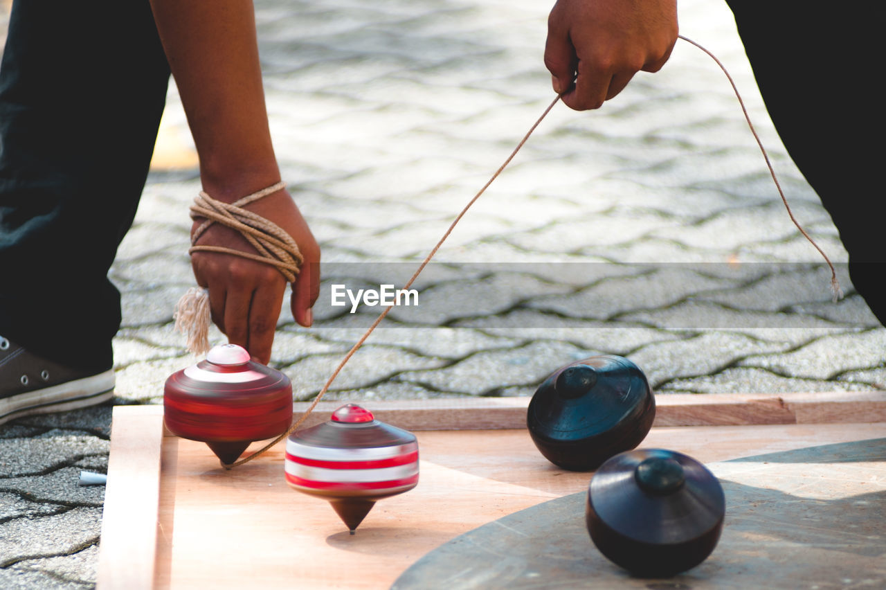 Low section of man playing with spinning top on wooden board over footpath