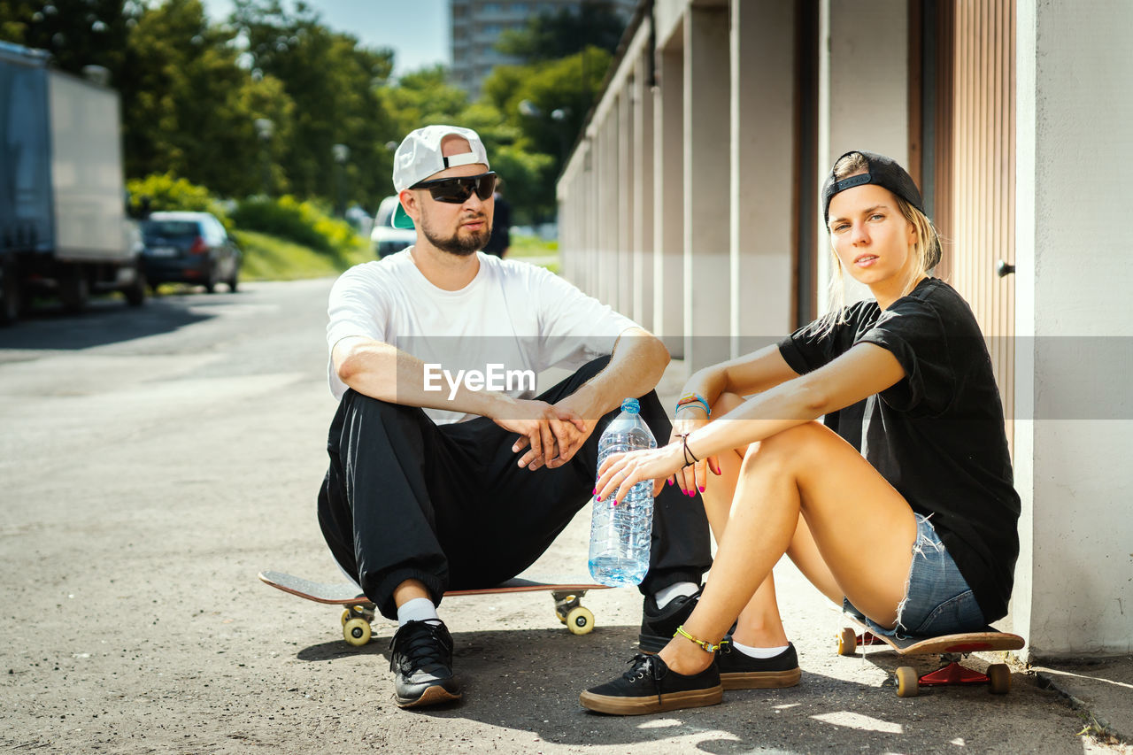 Portrait of couple with skateboards sitting in city