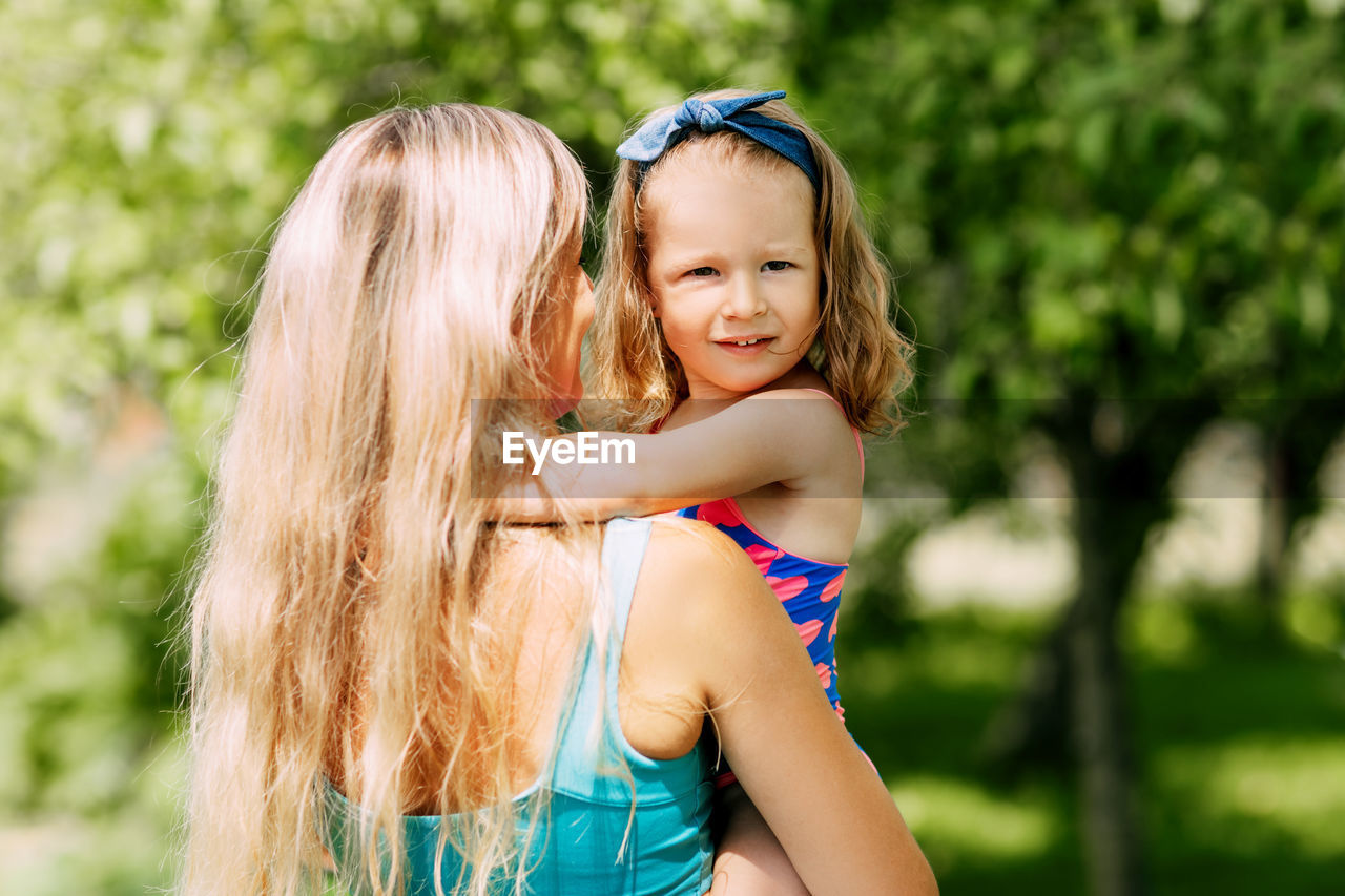 A young mother holds her little daughter in her arms on a summer day in the garden or park