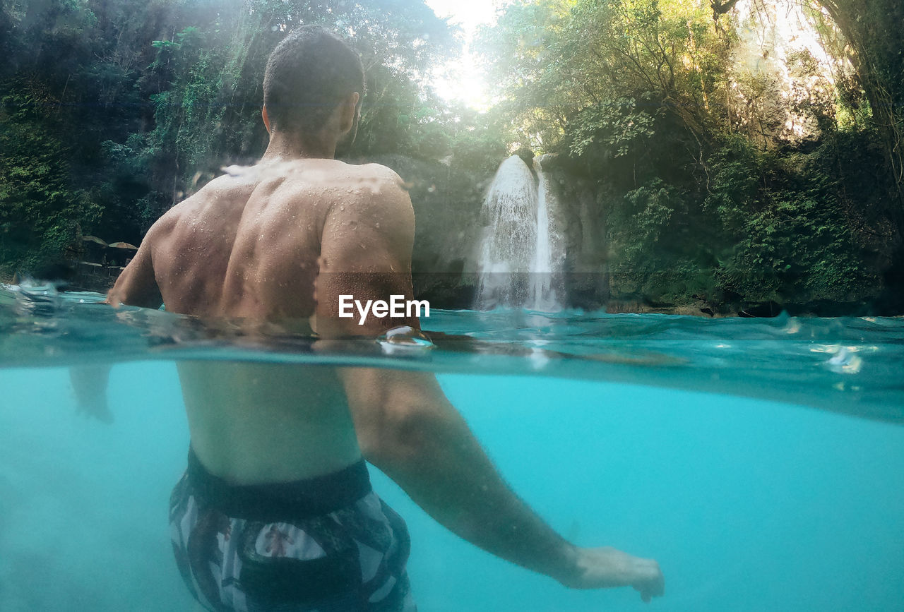 REAR VIEW OF MAN SWIMMING IN SEA