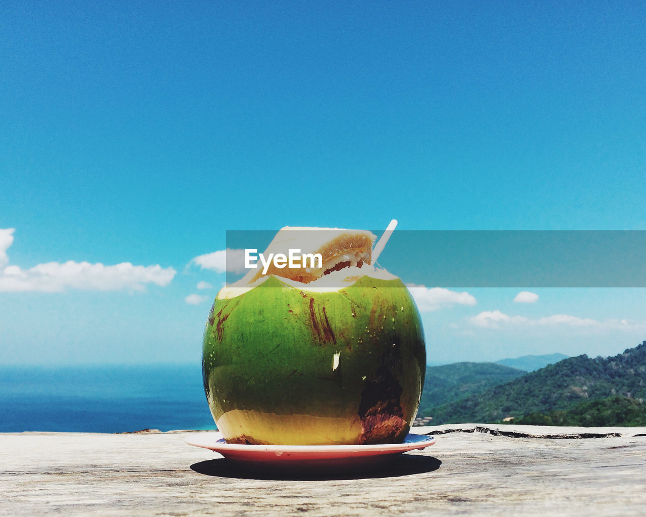 Coconut on table by sea and mountains against sky