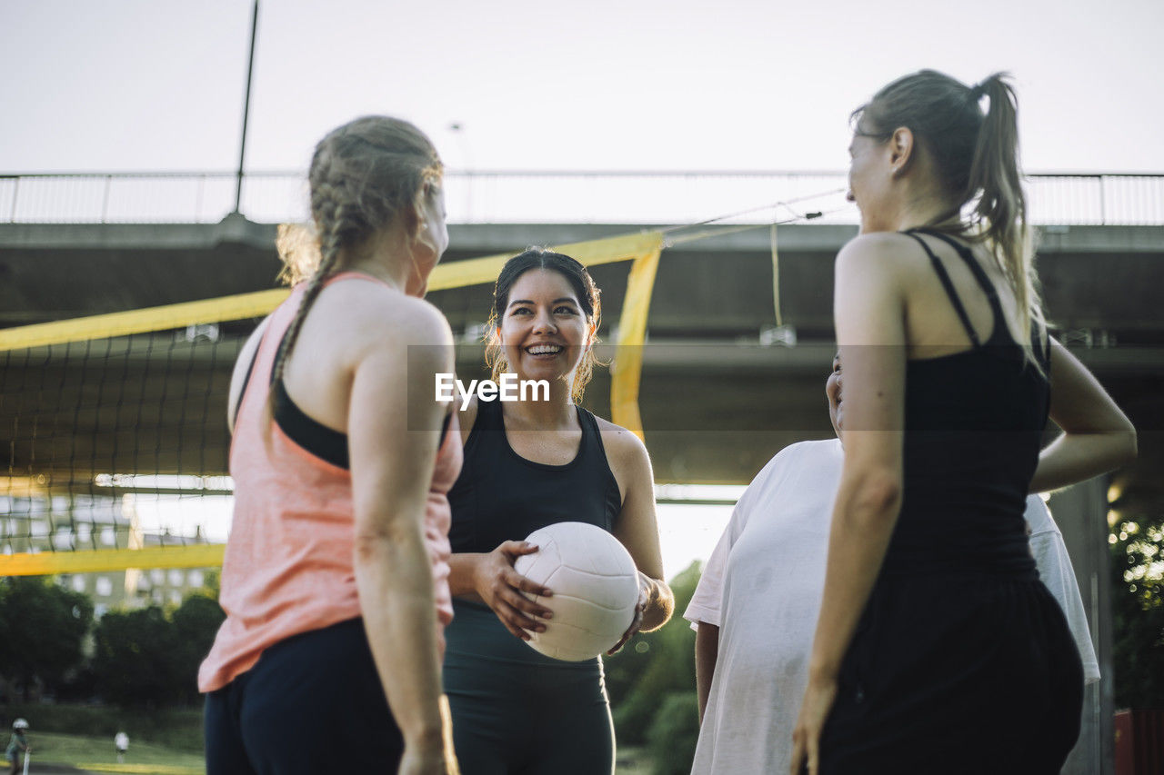Low angle view of smiling woman holding volleyball with female friends