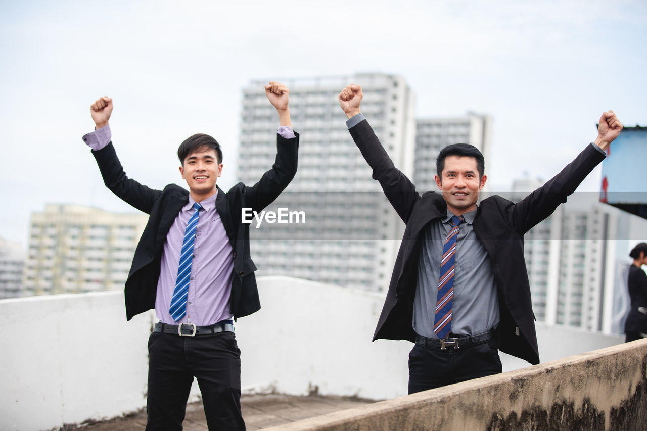 Portrait of business colleagues with arms raised while standing outdoors