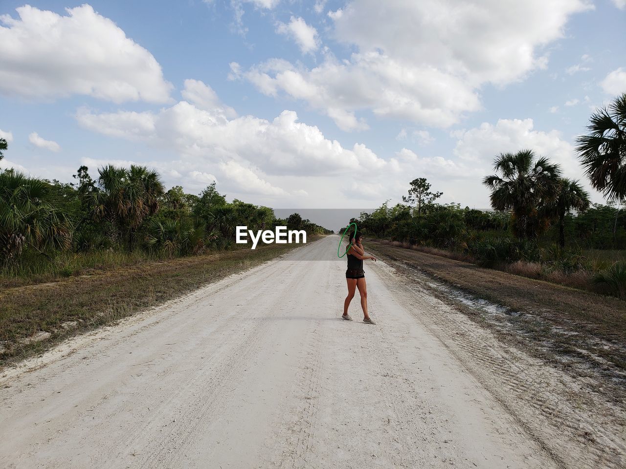 Woman standing on dirt road against cloudy sky