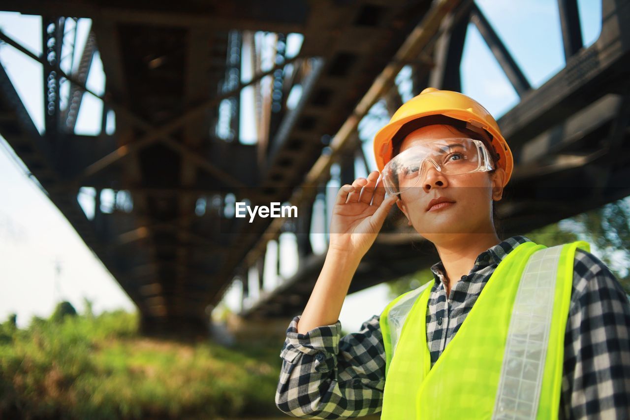 Engineer woman in hard hat holding walkie talkie while standing at construction site.