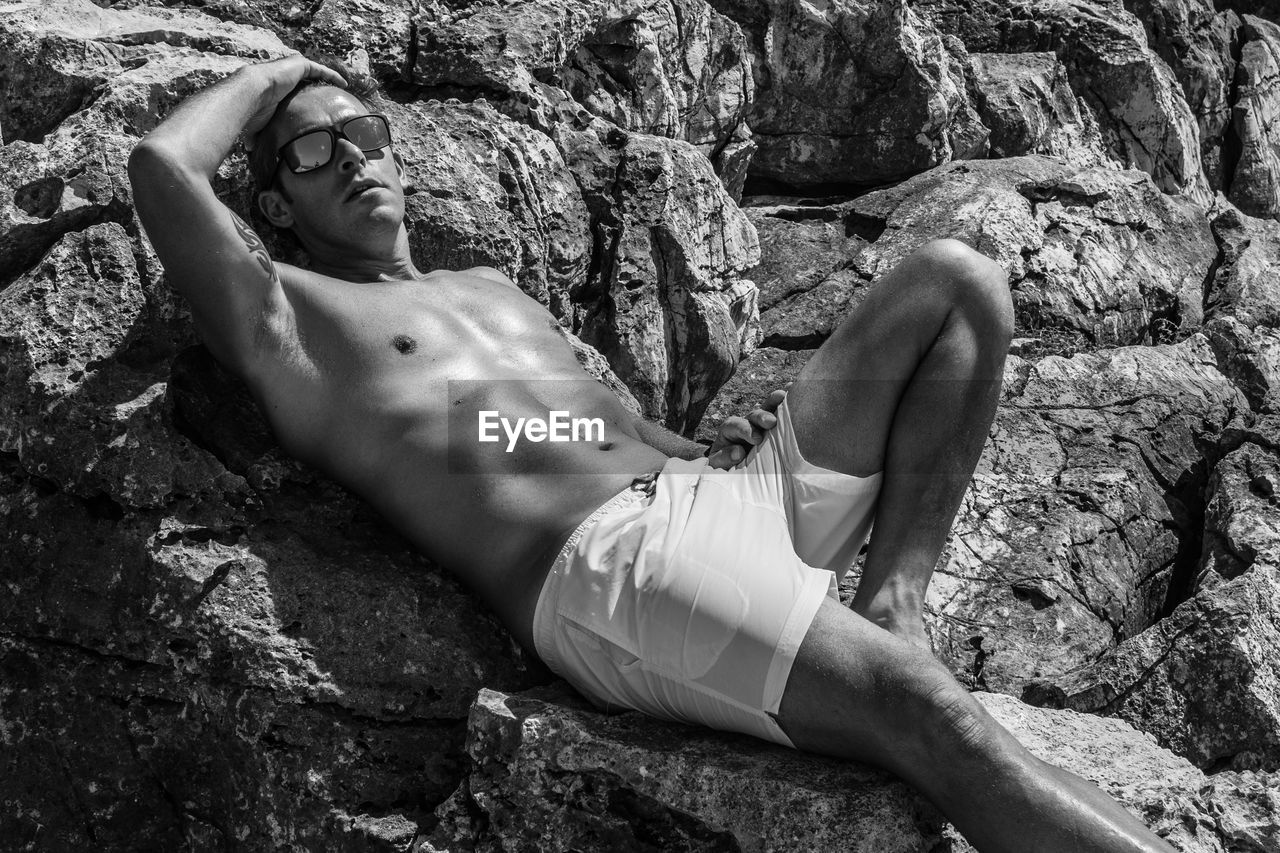 Shirtless man lying on rock formations