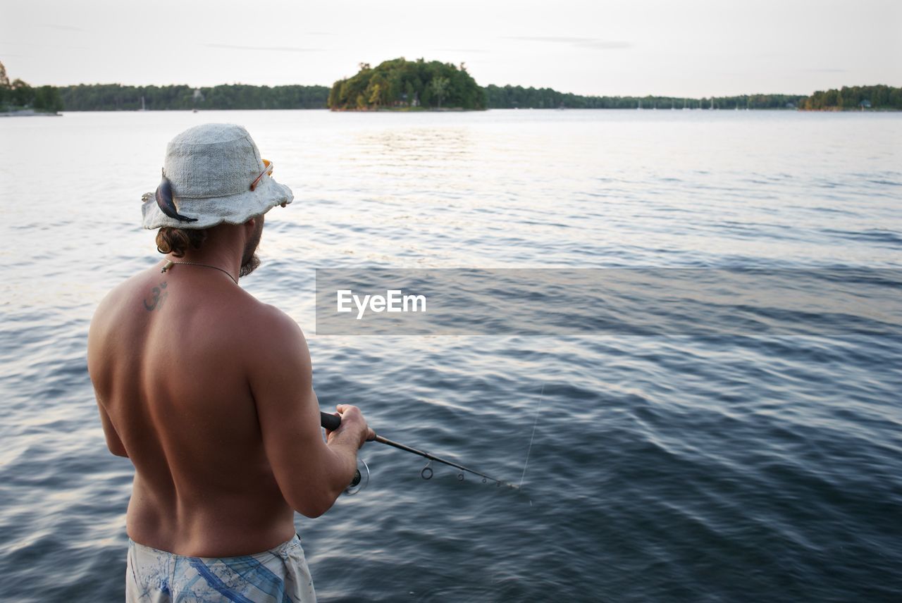 Rear view of shirtless man fishing in lake