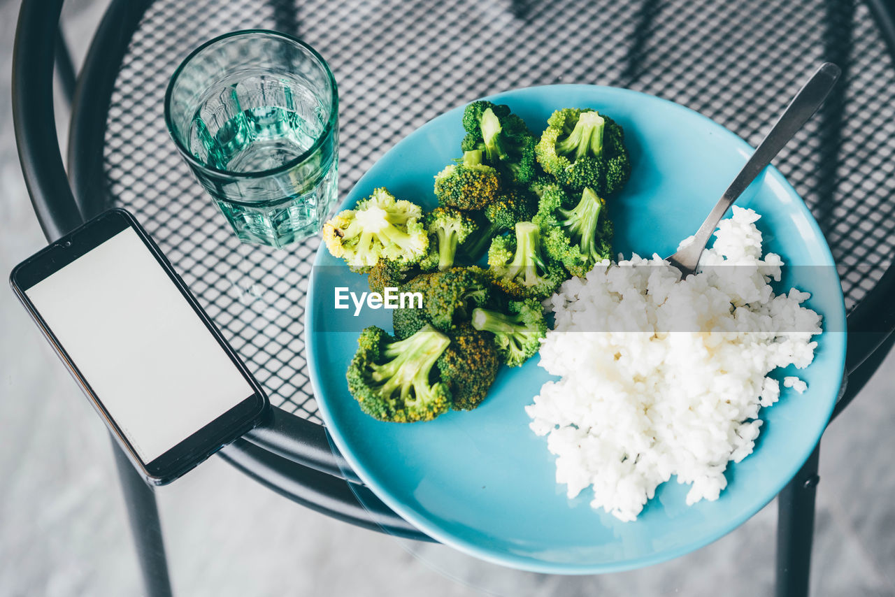 Using smart phone while eating broccoli and rice at home.