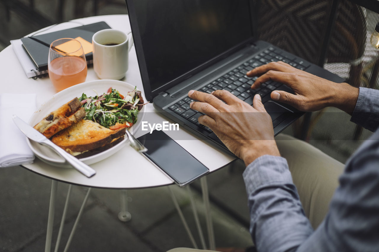 Hands of businessman using laptop by meal and smart phone on table