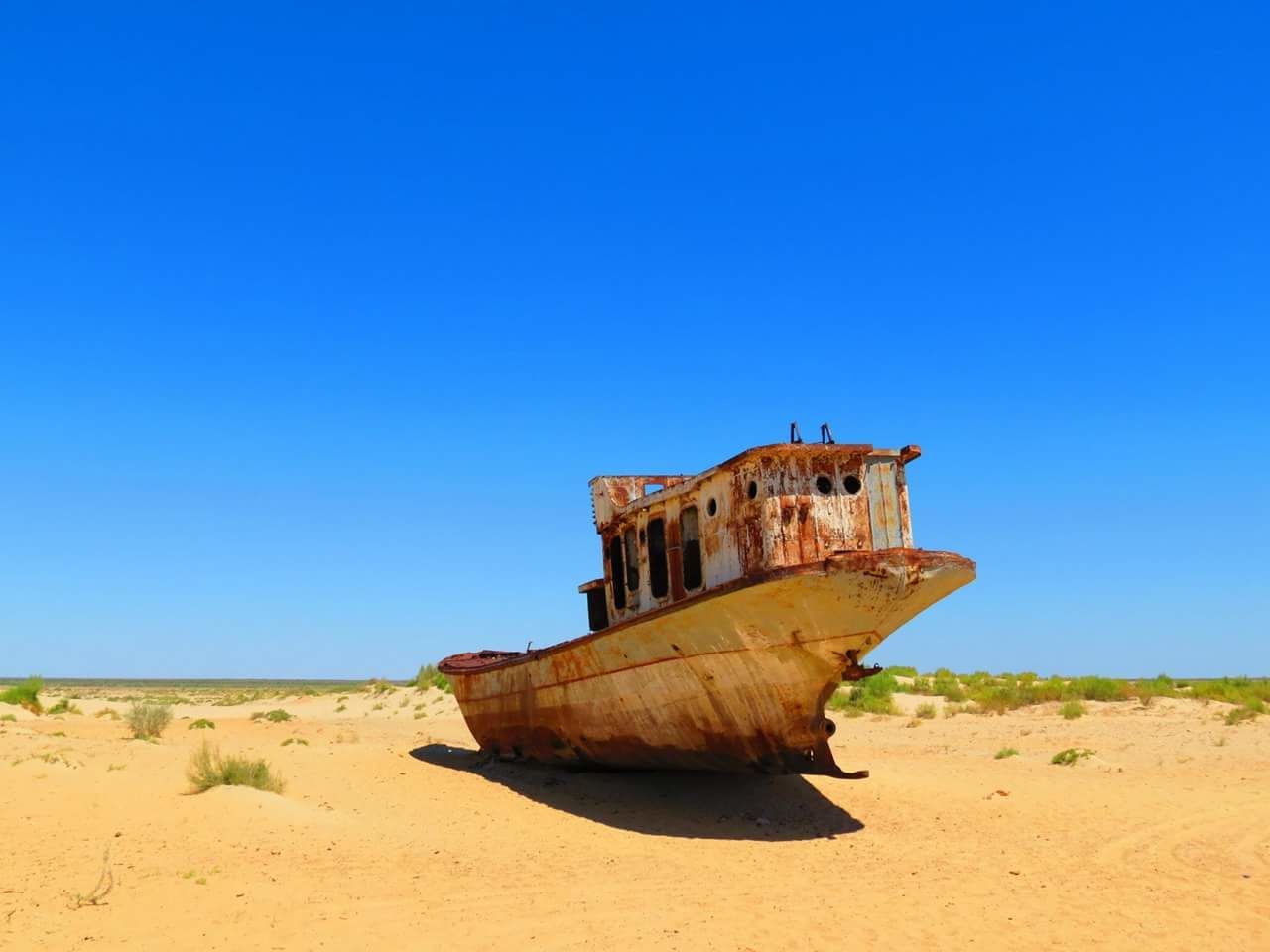 Abandoned boat on sand against clear blue sky