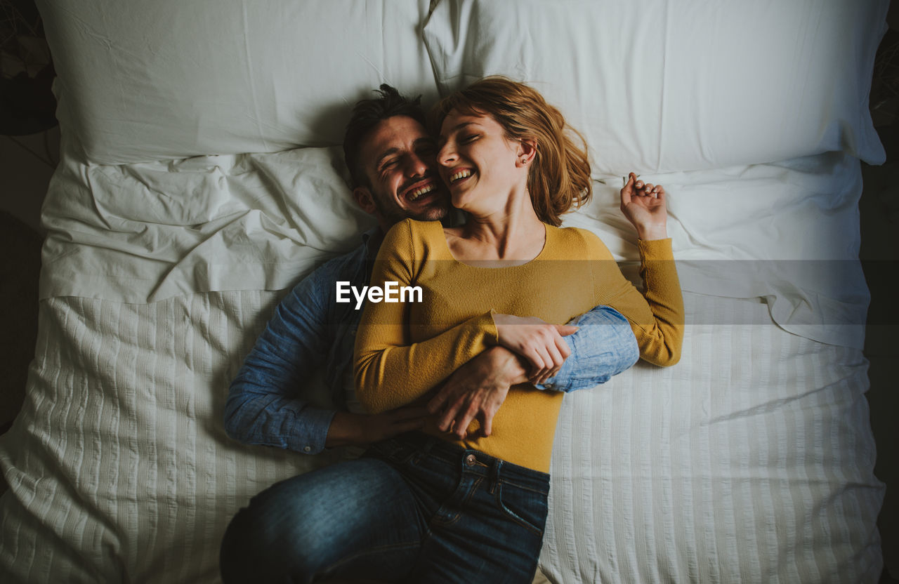 High angle view of couple embracing while lying on bed at home