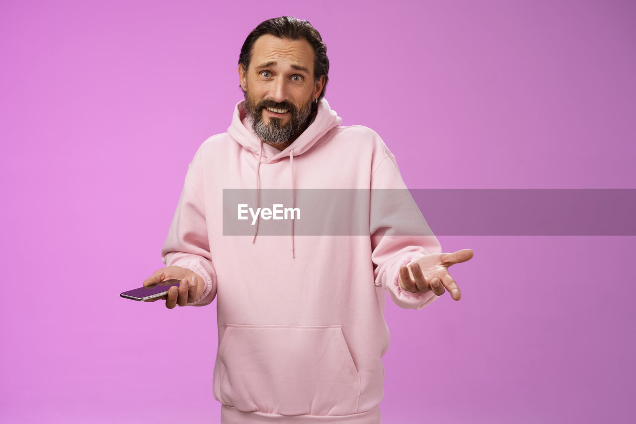 Clueless man holding smart phone against purple background