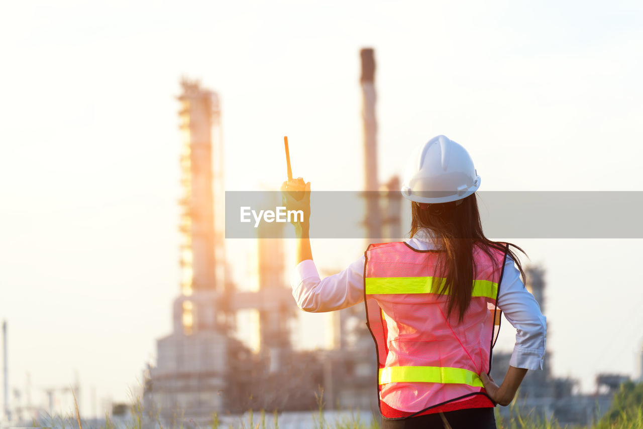 Rear view of engineer holding walkie-talkie against factory