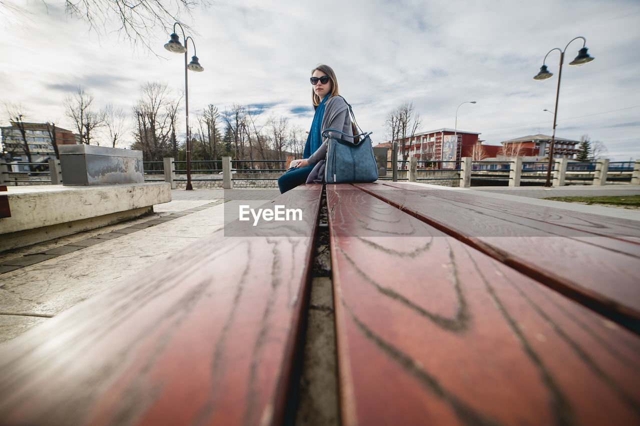 Side view of woman sitting on bench against sky