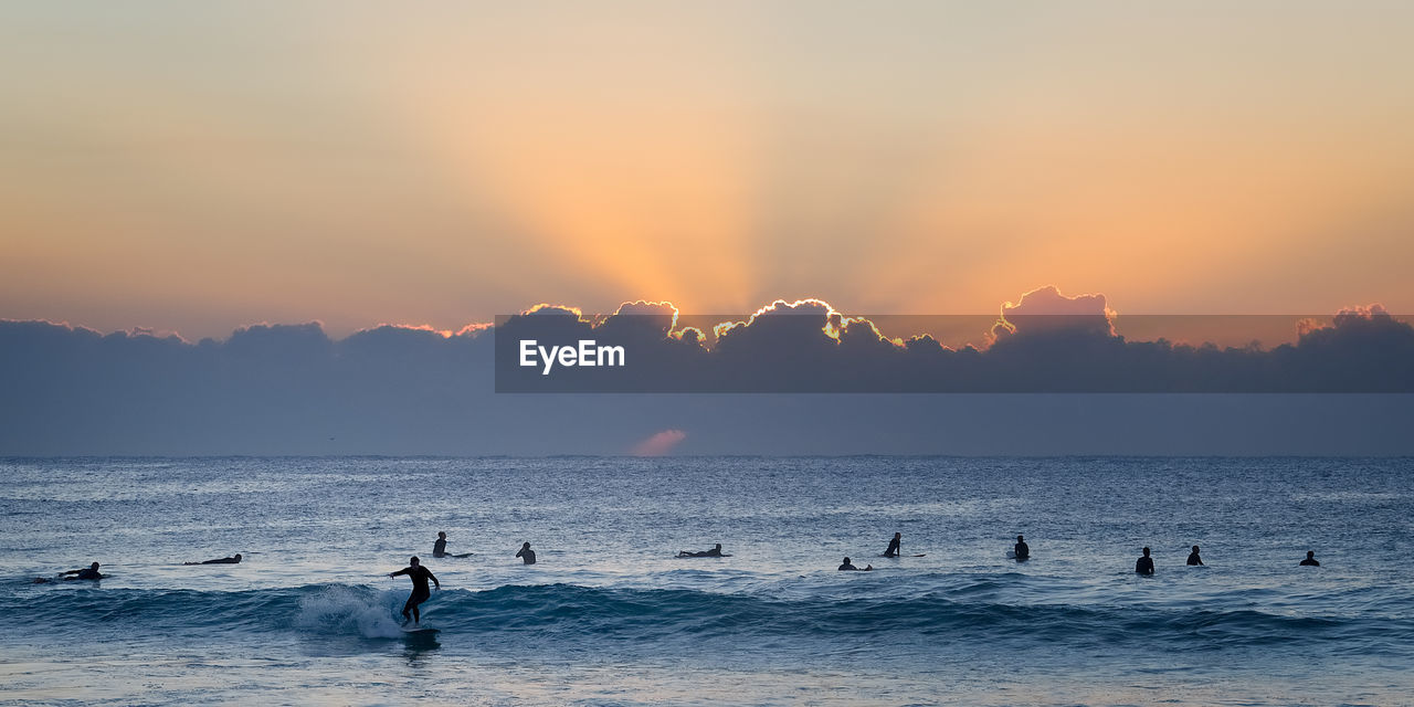 Silhouette people in sea against sky during sunset