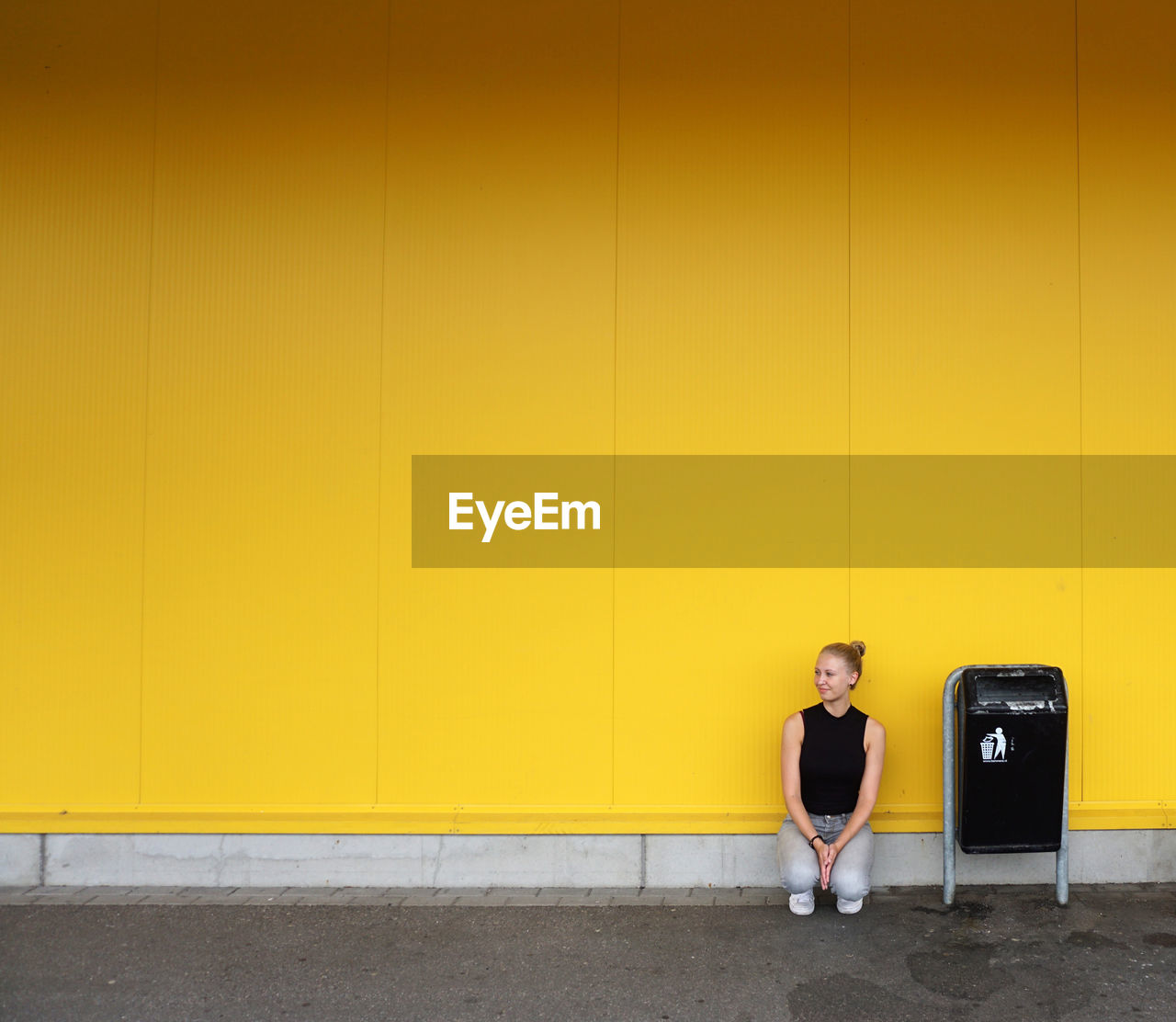 Woman crouching against yellow wall