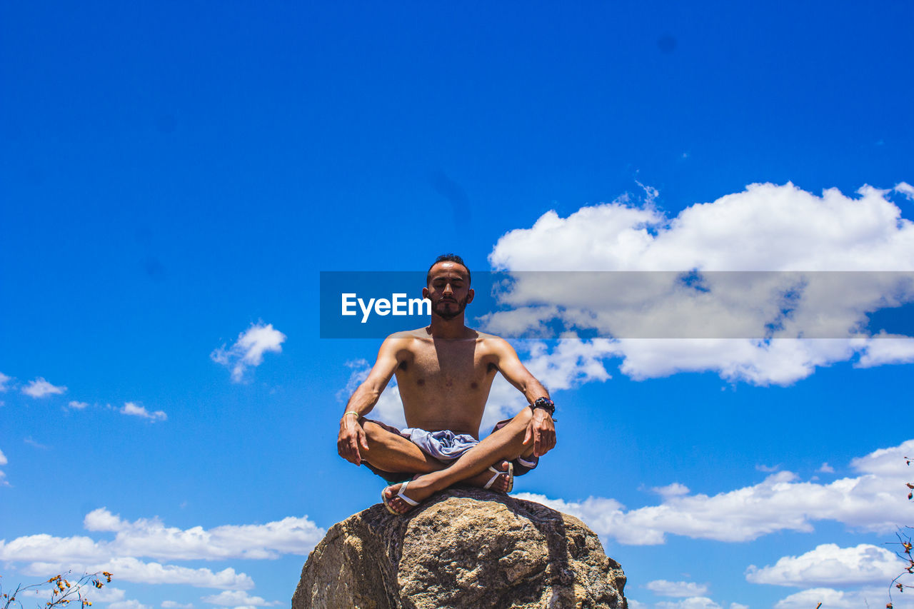 FULL LENGTH OF SHIRTLESS MAN STANDING AGAINST BLUE SKY