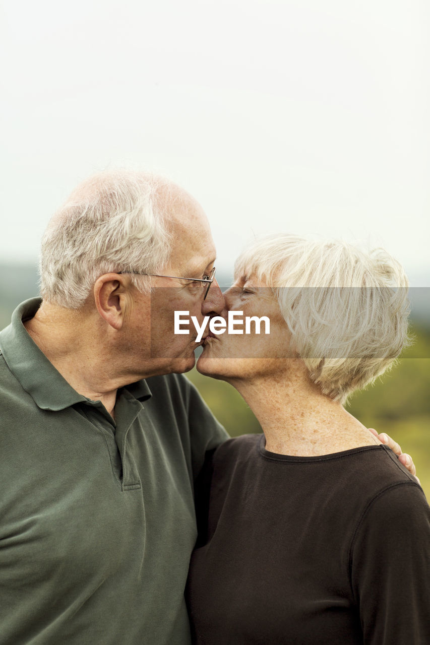 Affectionate senior couple kissing while standing against sky