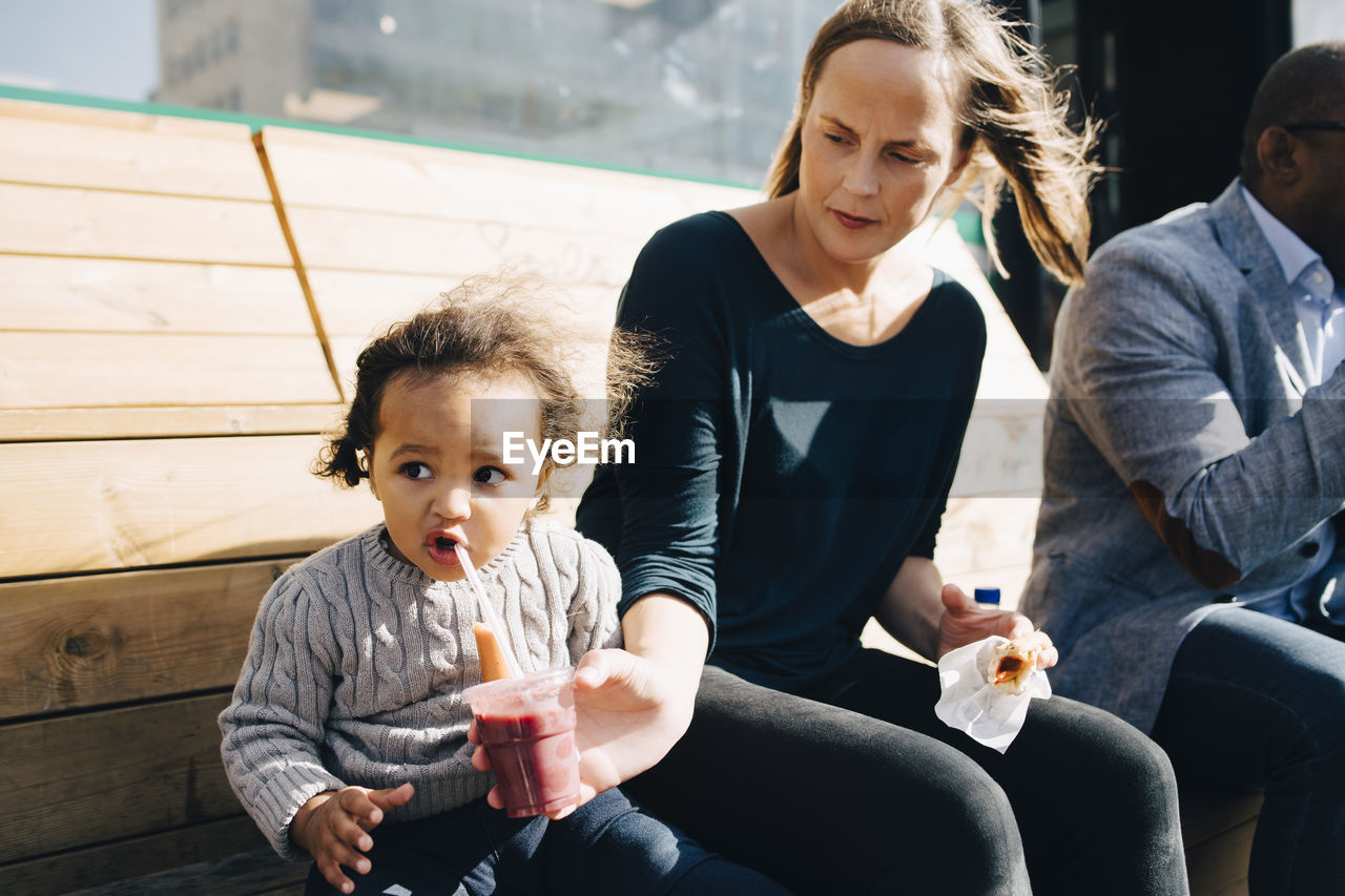 Woman sitting with man feeding drink to daughter while sitting at park