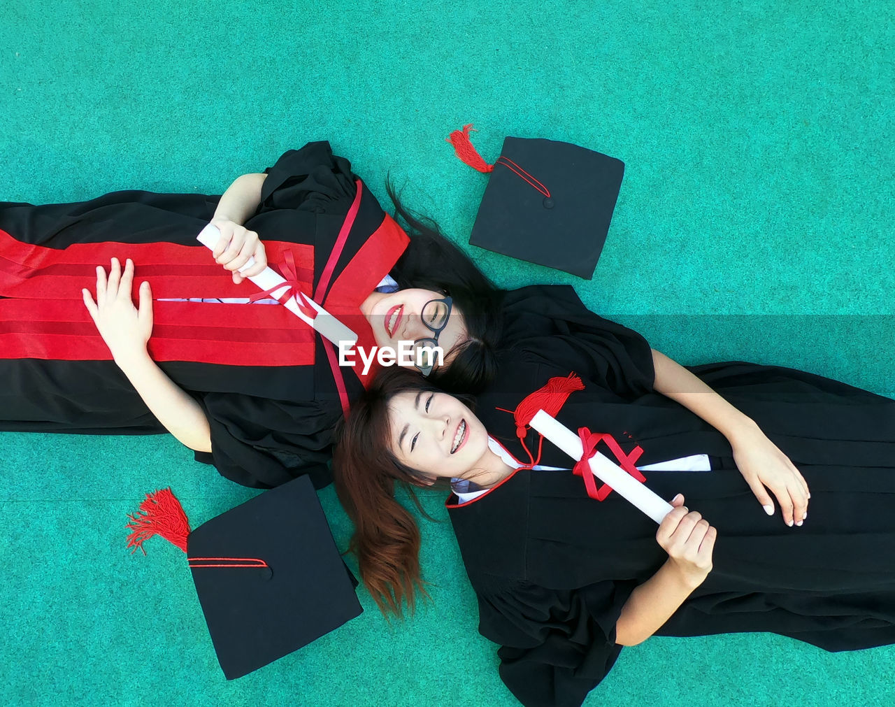 Portrait of friends in graduation gowns lying on floor