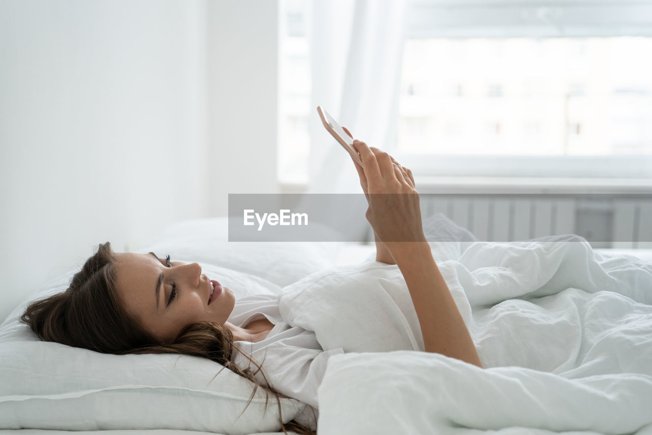 Woman using phone while lying on bed