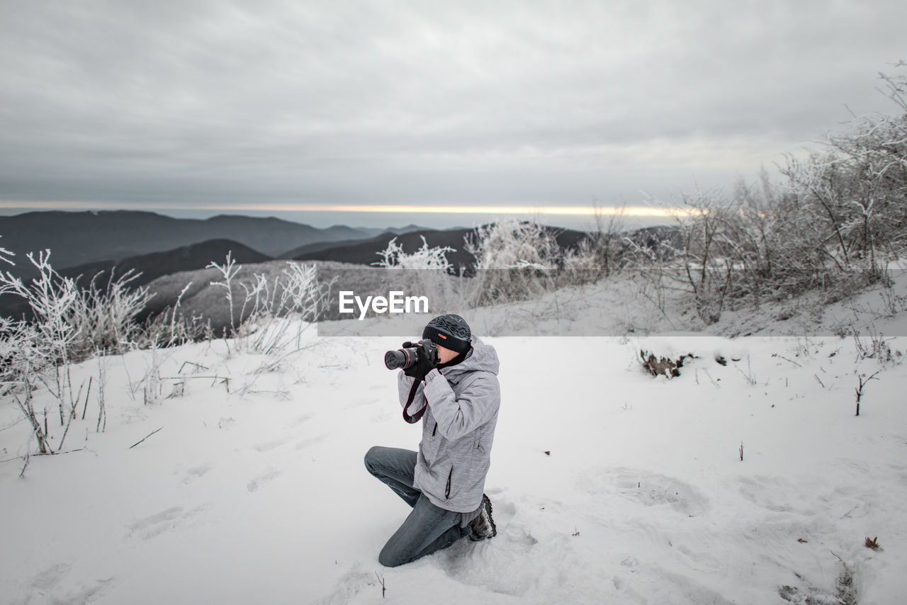 Man photographing while kneeling on snow covered landscape