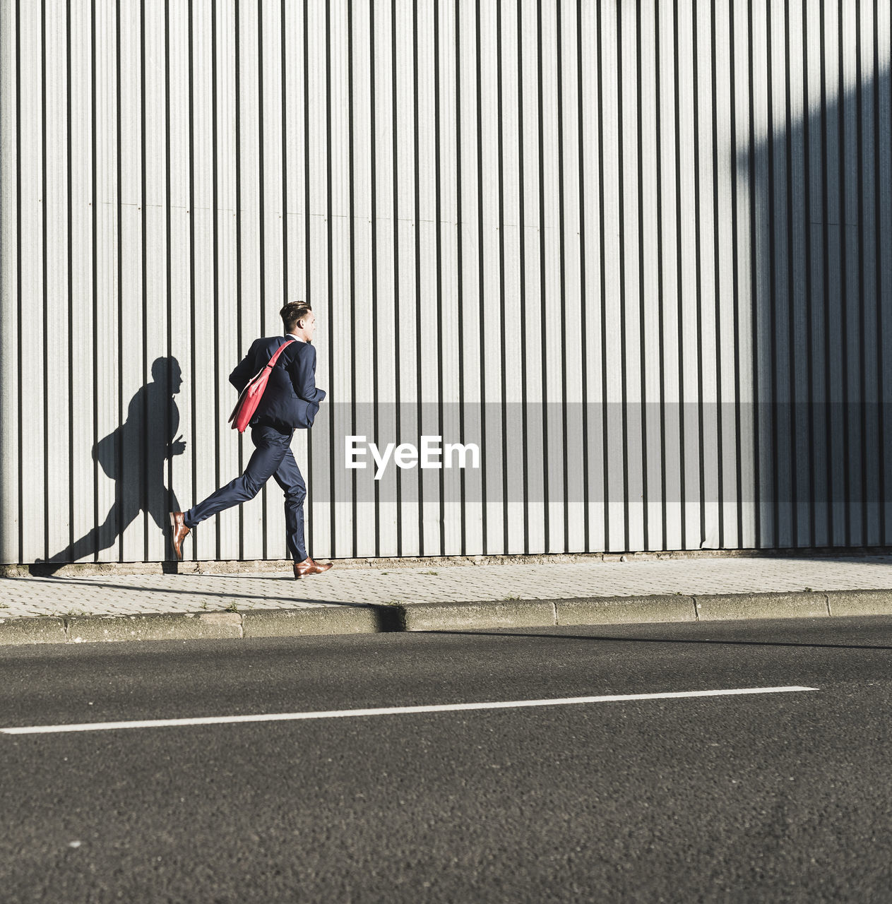 Young businessman running on pavement along building