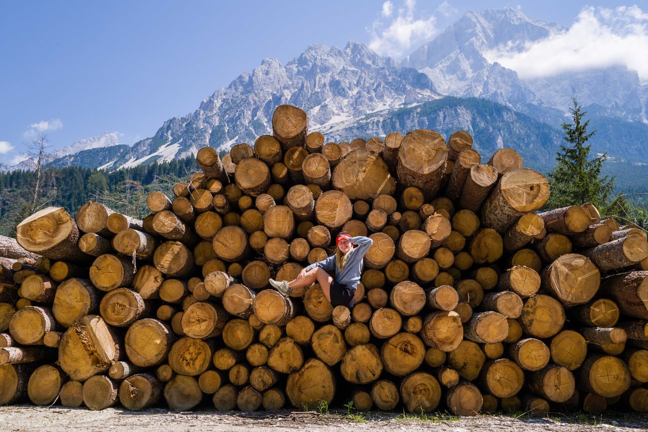 Woman sitting on the stack of the tree logs