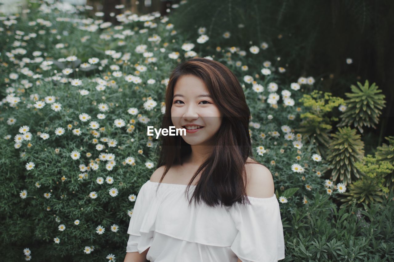 Portrait of smiling young woman by plants at public park