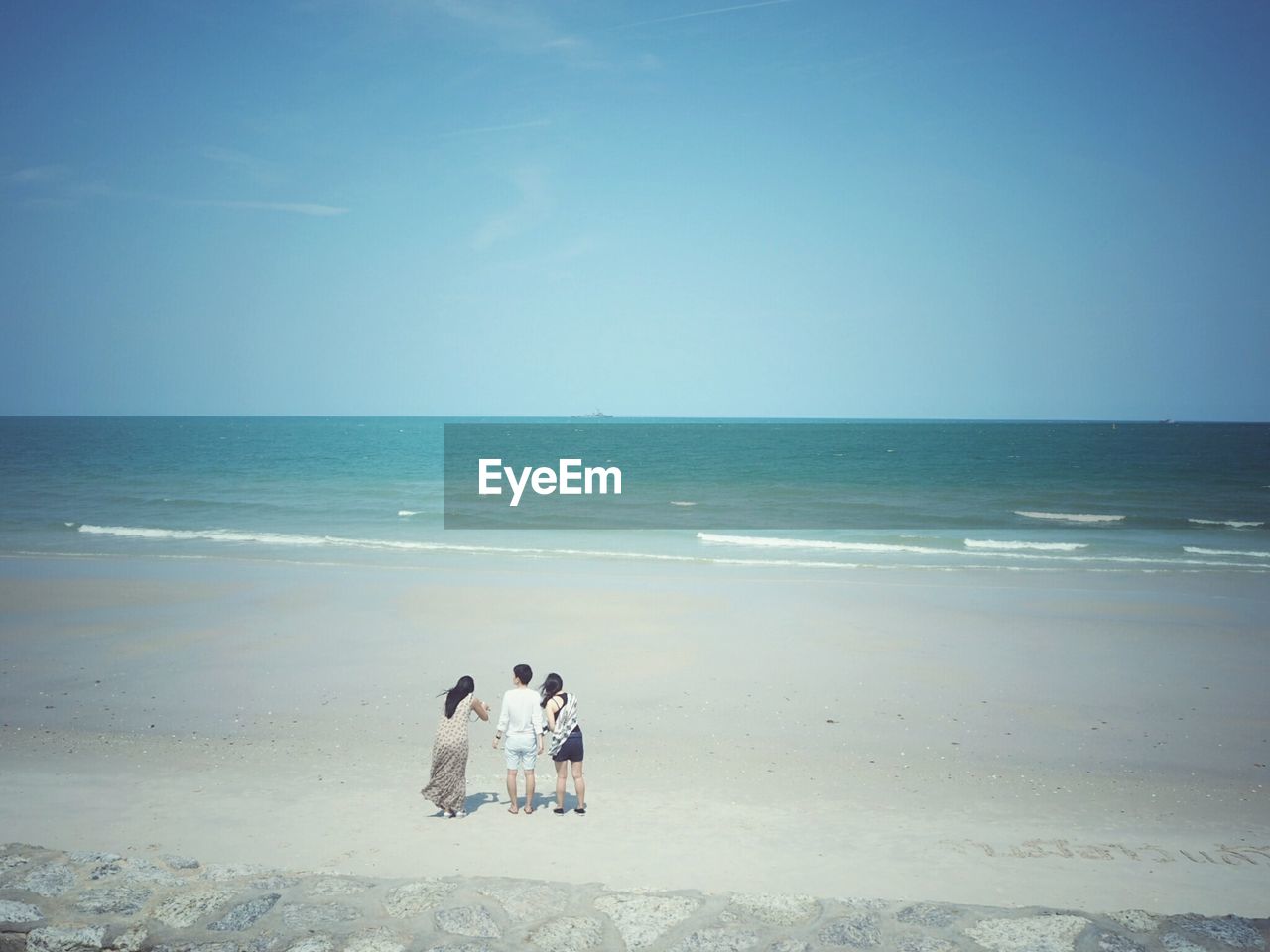 REAR VIEW OF PEOPLE ON BEACH AGAINST CLEAR SKY