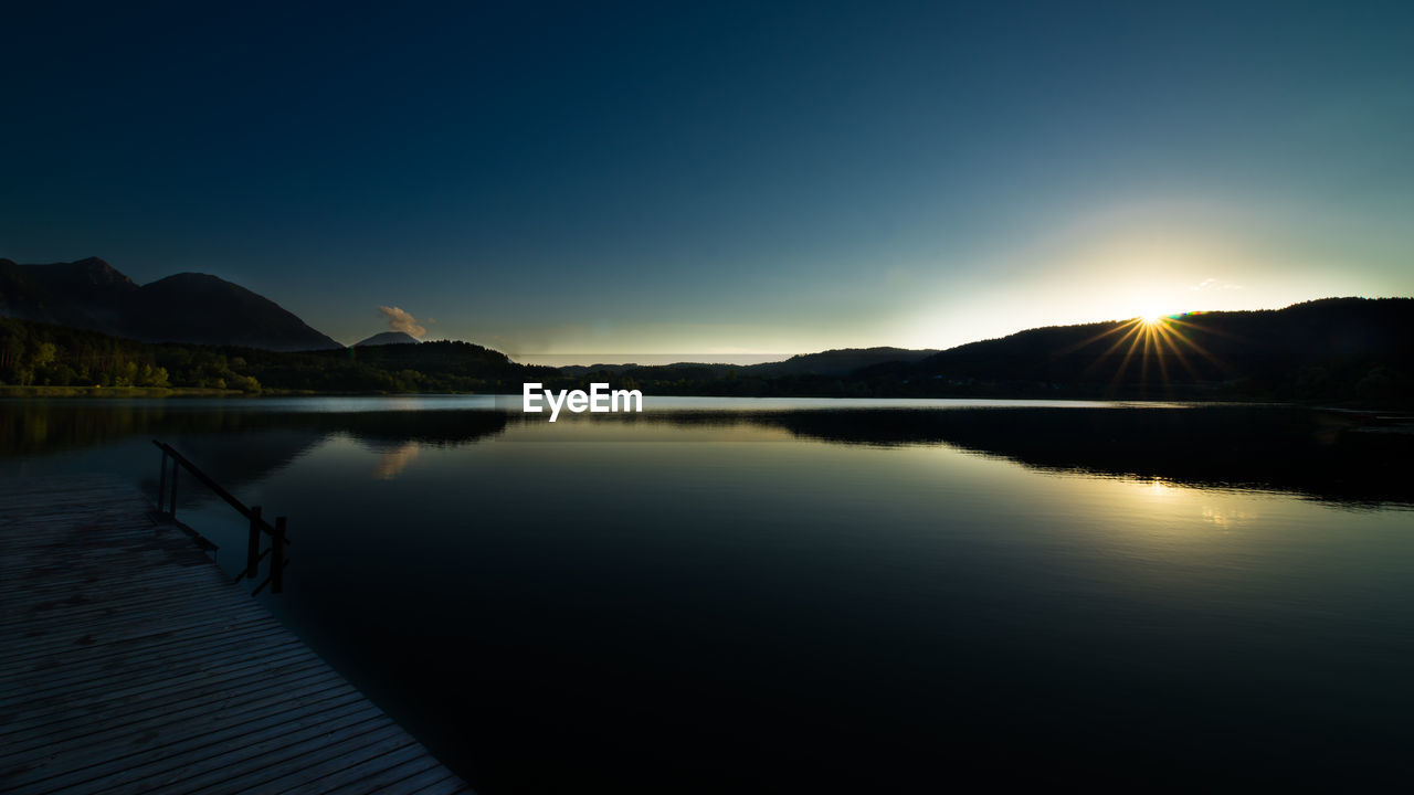 SCENIC VIEW OF LAKE AND MOUNTAINS AGAINST SKY AT SUNSET